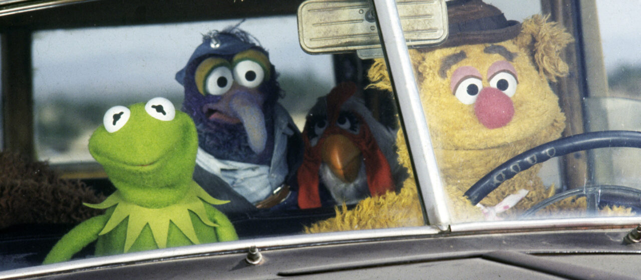 Three muppets sit in a car looking through the windshield.