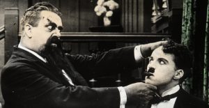 A man holds another man's head in a comic pose in a black and white image