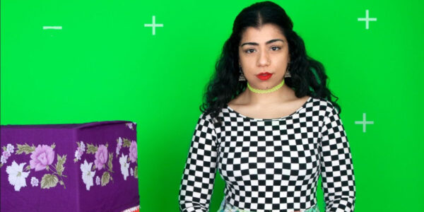 A woman stands against a stark green background wearing a black and white checked shirt