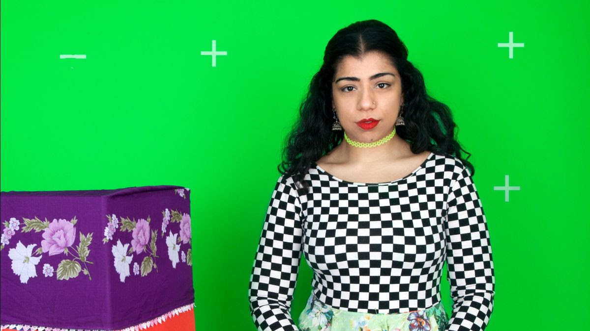 A woman stands against a stark green background wearing a black and white checked shirt