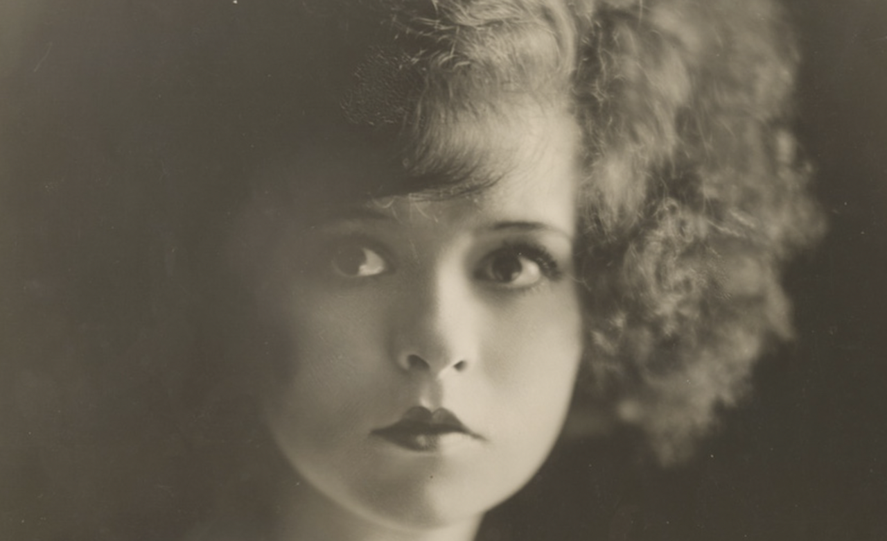 A black and white image of the silent star Clara Bow, with curly hair, looking at camera