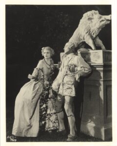 Rudolph Valentino romancing a woman in a hoop skirt by a fountain