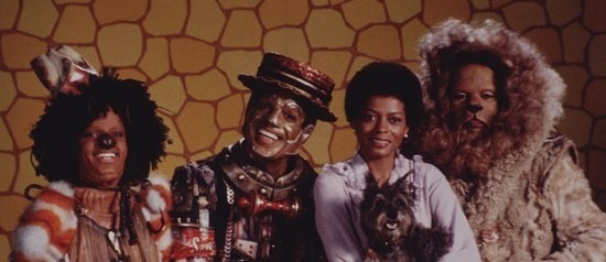 Four cast members of The Wiz, including Dorothy holding her little dog Toto, look at the camera and smile.