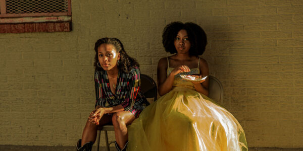 A mother and daughter sitting side by side looking at camera, the younger woman in a pageant dress.
