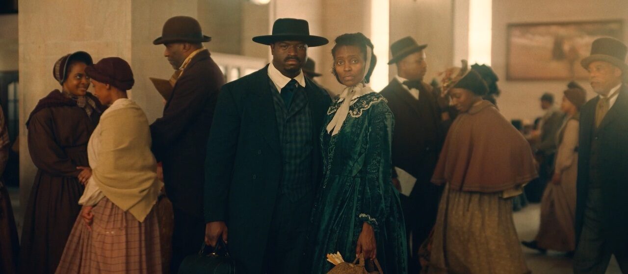 A man and woman in period dress stare directly at camera