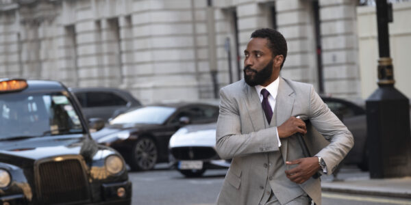 A man in a grey business suit reached into his breast pocket while walking on a street