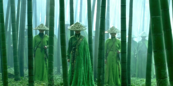 A line of emerald green-dressed assassins, their faces hidden under hats, stands in a bamboo forest facing the camera