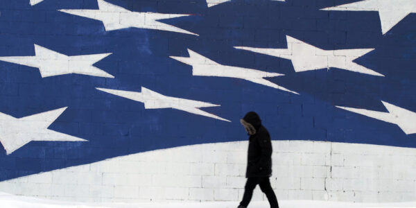 A man in silhouetted walks past the stars of a huge American flag