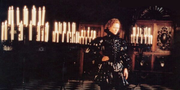 An androgynous English poet of the Elizabethan era stands in a dark room full of lit candles.