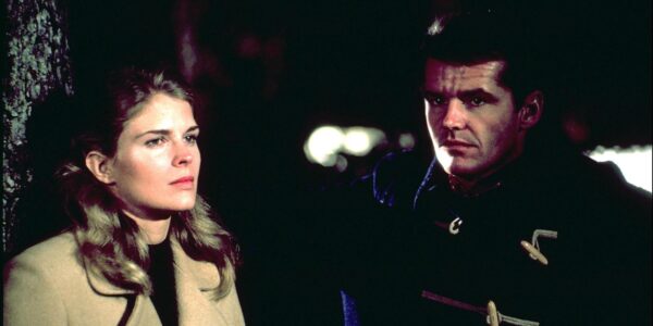 A man and woman stand outside on a dark street, not quite looking at each other.