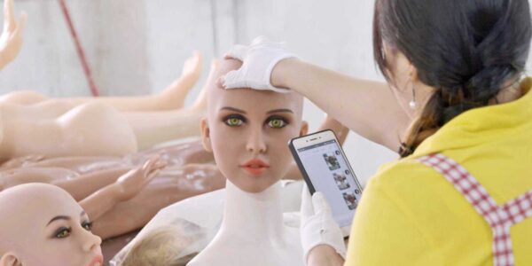 A factory worker holds the head of a plastic mannequin, which is directly facing the camera.