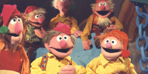 Muppet elves in yellow shirts smiling at the camera