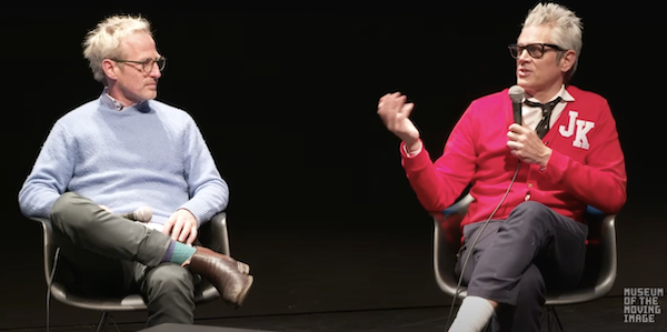 Spike Jonze in white and Johnny Knoxville in red, sitting on stage at the Museum, talking.