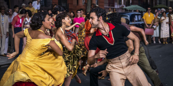 A dancing woman and man in bright yellow and red-trimmed dress and red and black shirt on a sidewalk