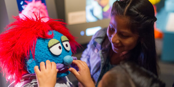 A young girl and a tour guide touch a muppet