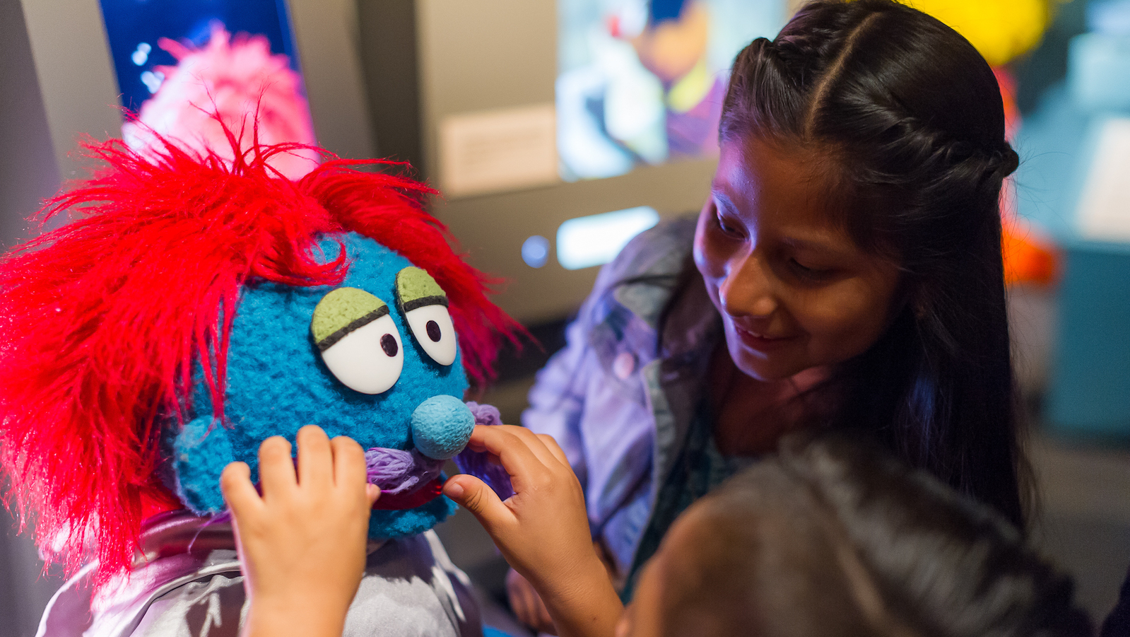 A young girl and a tour guide touch a muppet