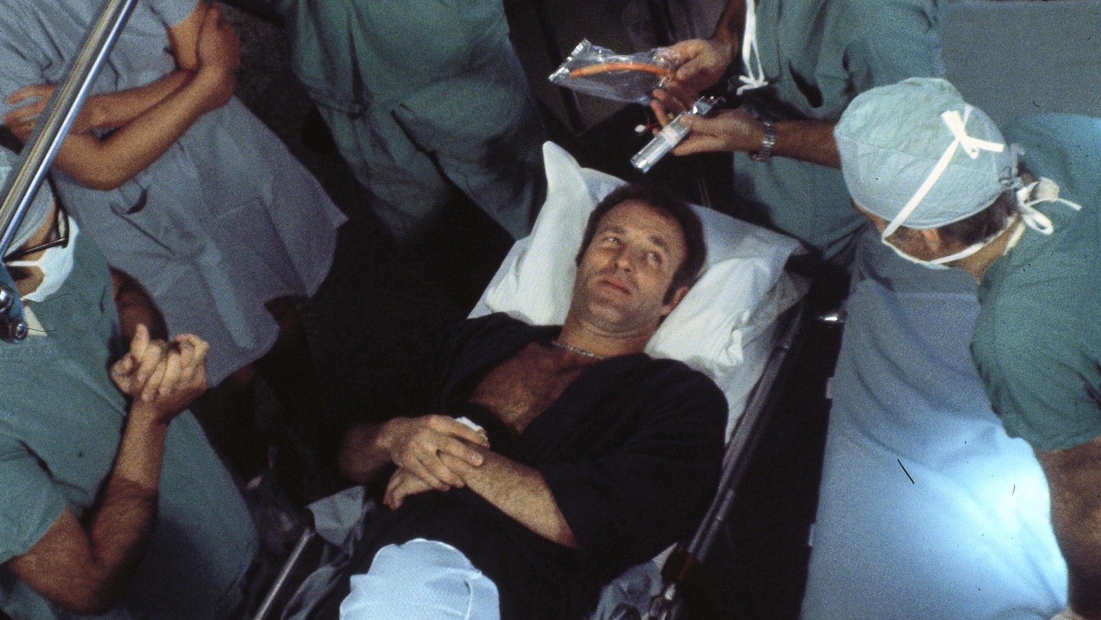 An overhead shot of a man , awake, on a surgery table surrounded by doctors