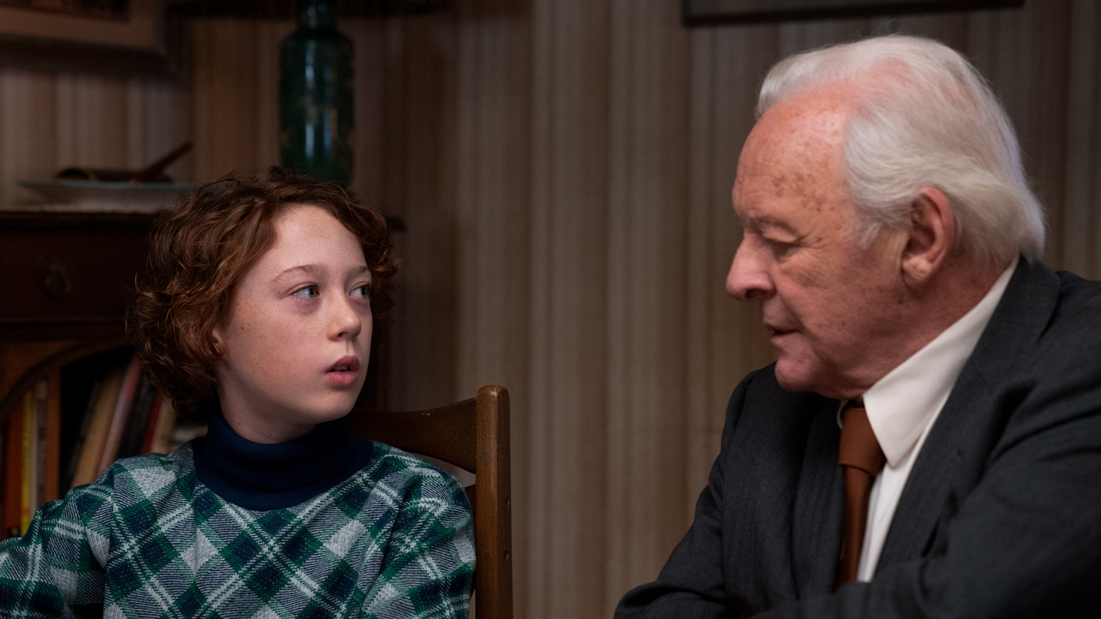 A young boy and his grandfather look at each other at the dinner table.