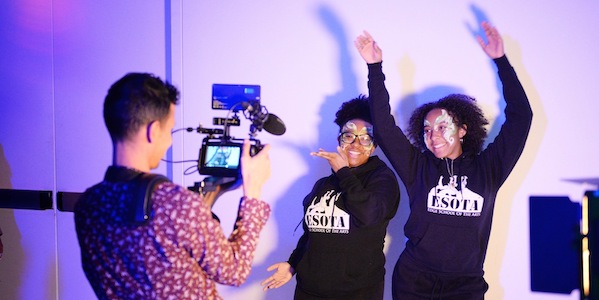 Two young women in facepaint joyously dancing in front of a camera