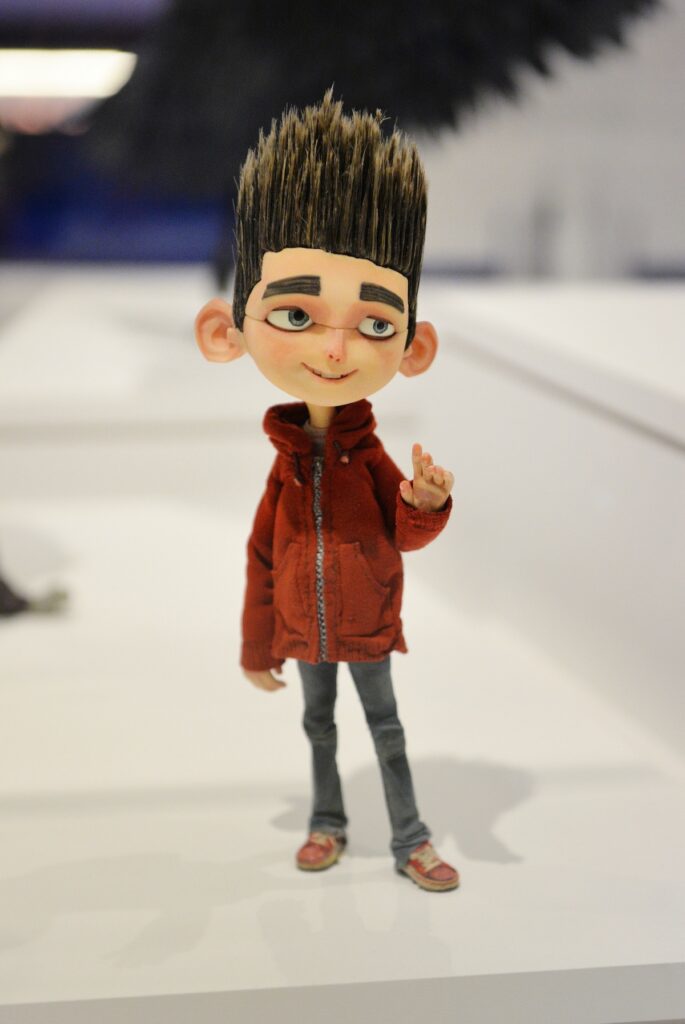 a figure of a pale-faced boy wearing a reddish hoodie, jeans, and sneakers. His hair stands on end. He is smiling and reaching out with his hand.