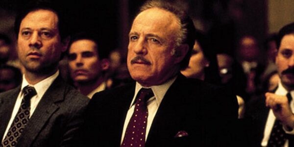 A man sits in a courtroom in a suit and looks serious.