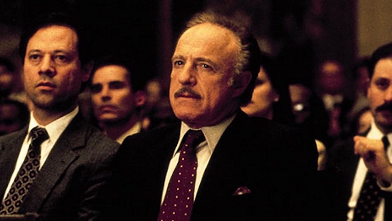 A man sits in a courtroom in a suit and looks serious.