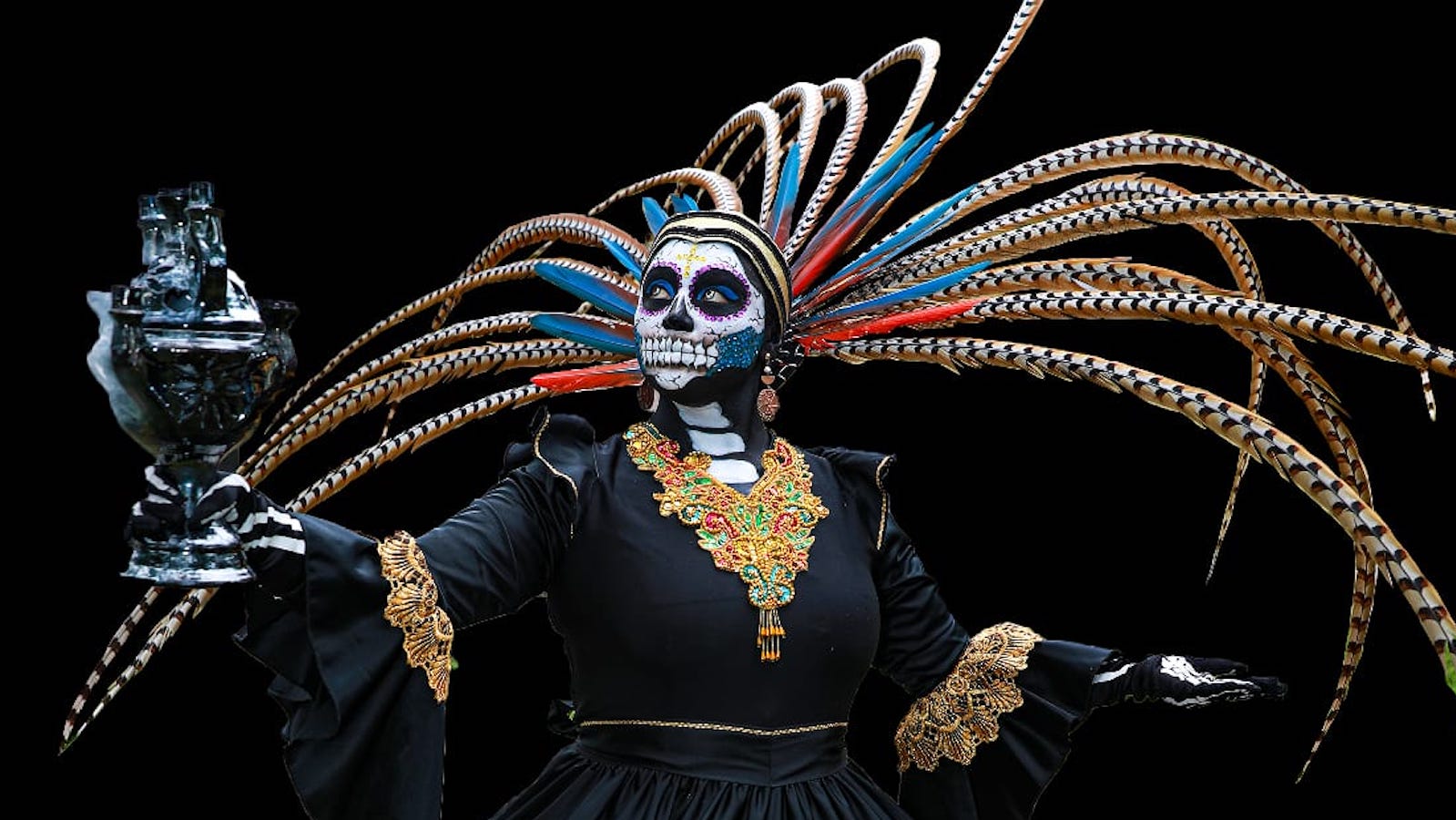 A person in a colorful costume and skeleton mask with feathers
