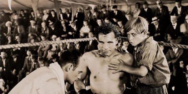 A boxer in the ring, looking at camera, beside a kid and his trainer.