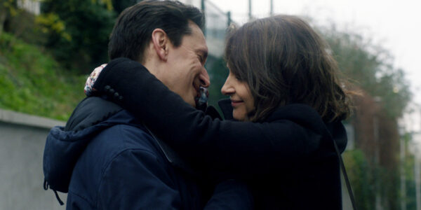 A man and woman hug each other and smile surrounded by green trees
