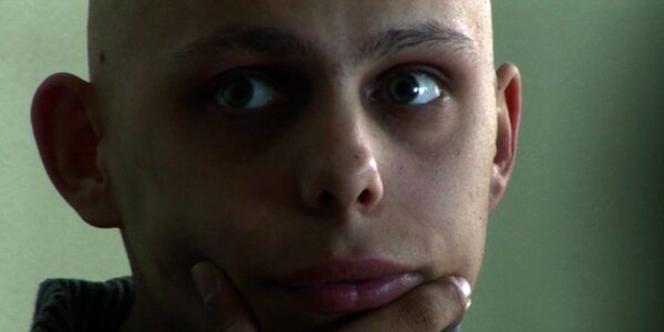 A person in intense close-up, looking off-screen while gripping their chin pensively and with wide eyes.