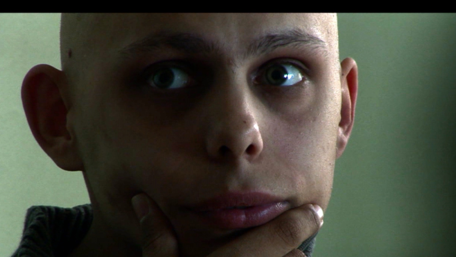 A person in intense close-up, looking off-screen while gripping their chin pensively and with wide eyes.