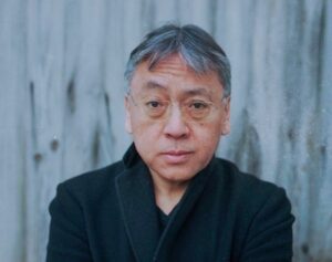 A man in rimless glasses looks directly at camera in a black shirt against a gray background