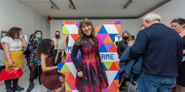 A woman in a pink and purple dress smiles and poses in front of a multicolored arcade console