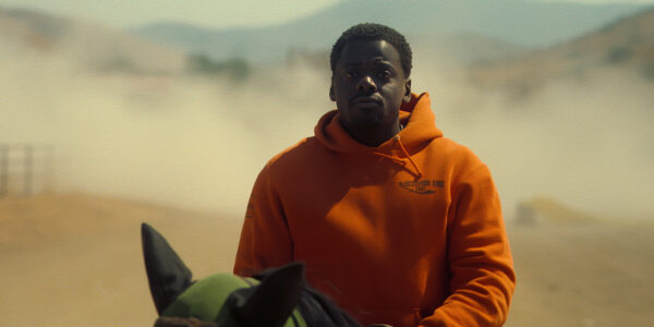 A man in an orange hoodie sweatshirt on a horse in a desert