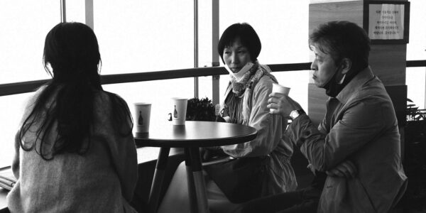 A woman with a facemask dangling on her chin sits at a restaurant with a man and a woman