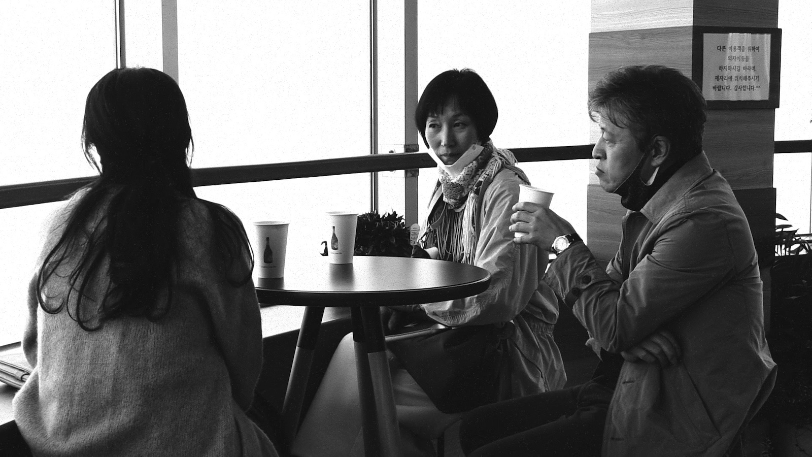 A woman with a facemask dangling on her chin sits at a restaurant with a man and a woman