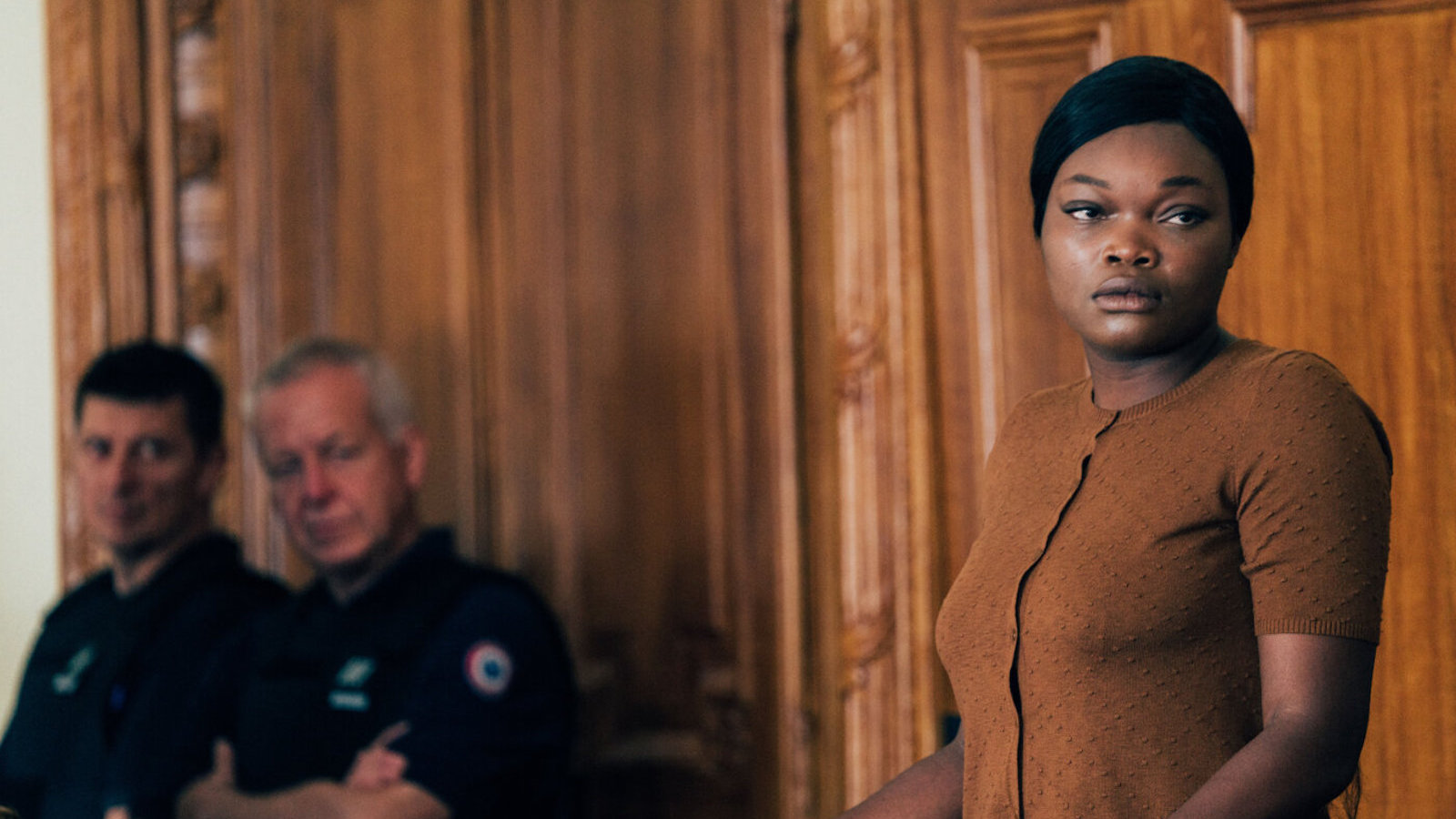 A woman in beige stands in a courtroom