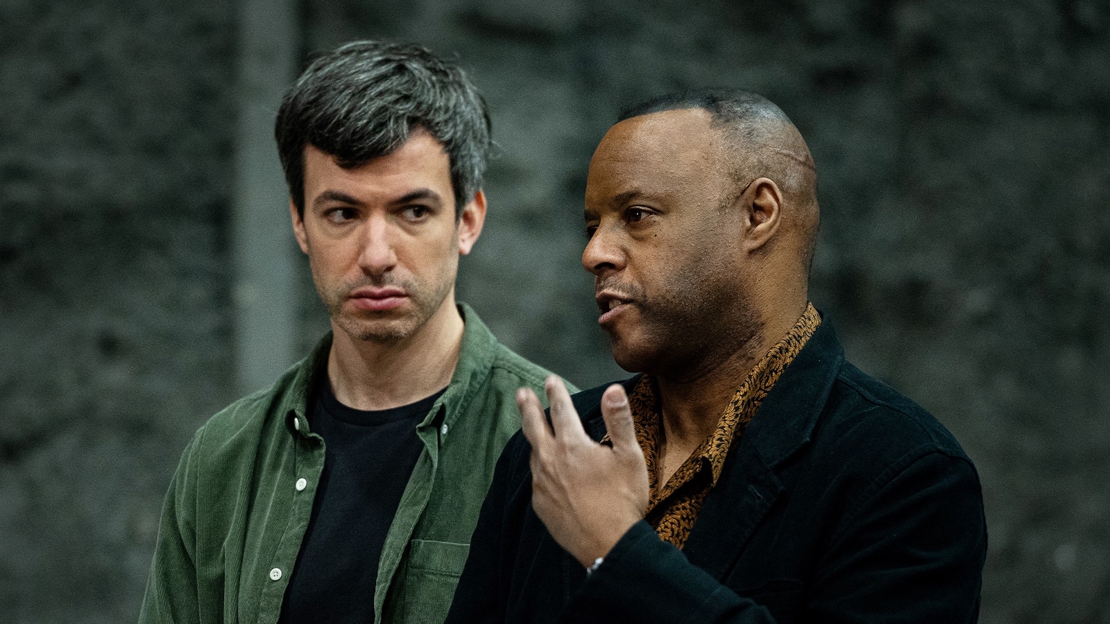 Two men in conversation, one in foreground talking, the other looking at him intently