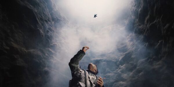 A man reaches up in the middle of a cave at floating leaves above his head