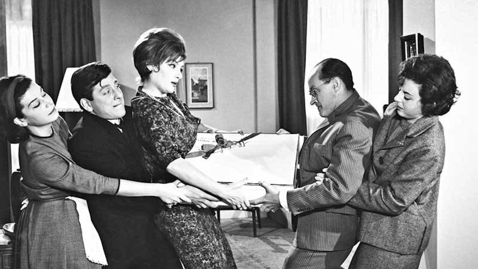 A black and white photo of five people fighting over a large paper gift box, three people on the left and two on the right