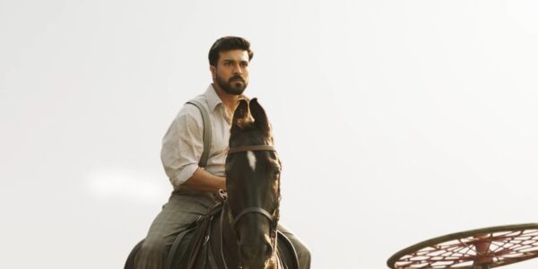 A bearded man in suspenders and a white shirt rides on horseback towards camera