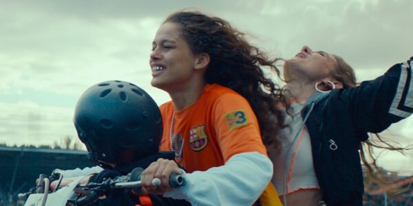 Two young women on a motorcycle, the one in back with arms in air