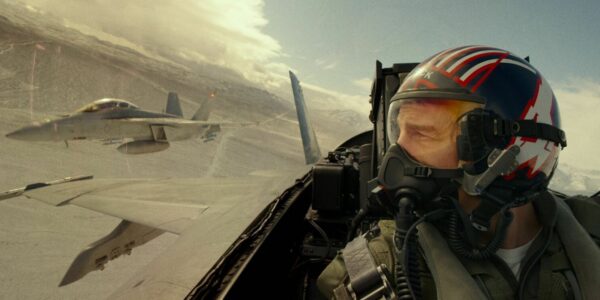 A navy pilot in helmet and mask flies in his cockpit while enemy planes fly close-by in the sky to his left