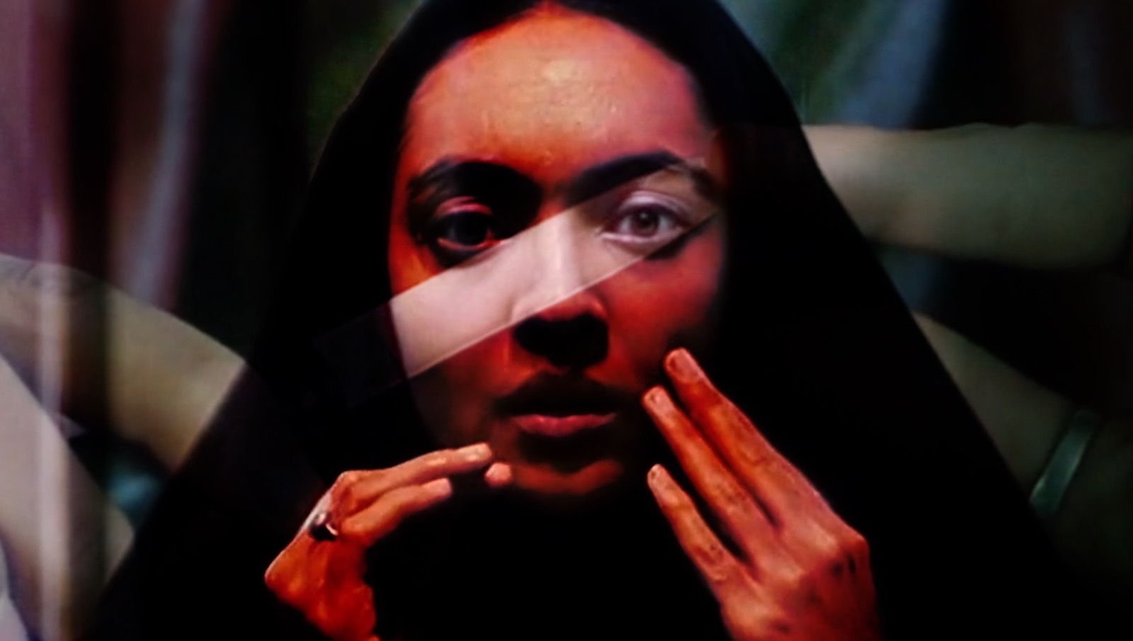 A woman in a hijab looks at the camera in closeup and touches her face