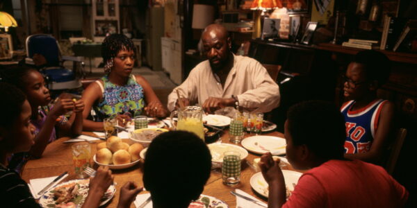 A family sits around a dinner table, with the parents in the back center of the frame