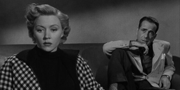 A woman in the foreground looks off screen concerned, while a man sits behind her on the same couch looking at her