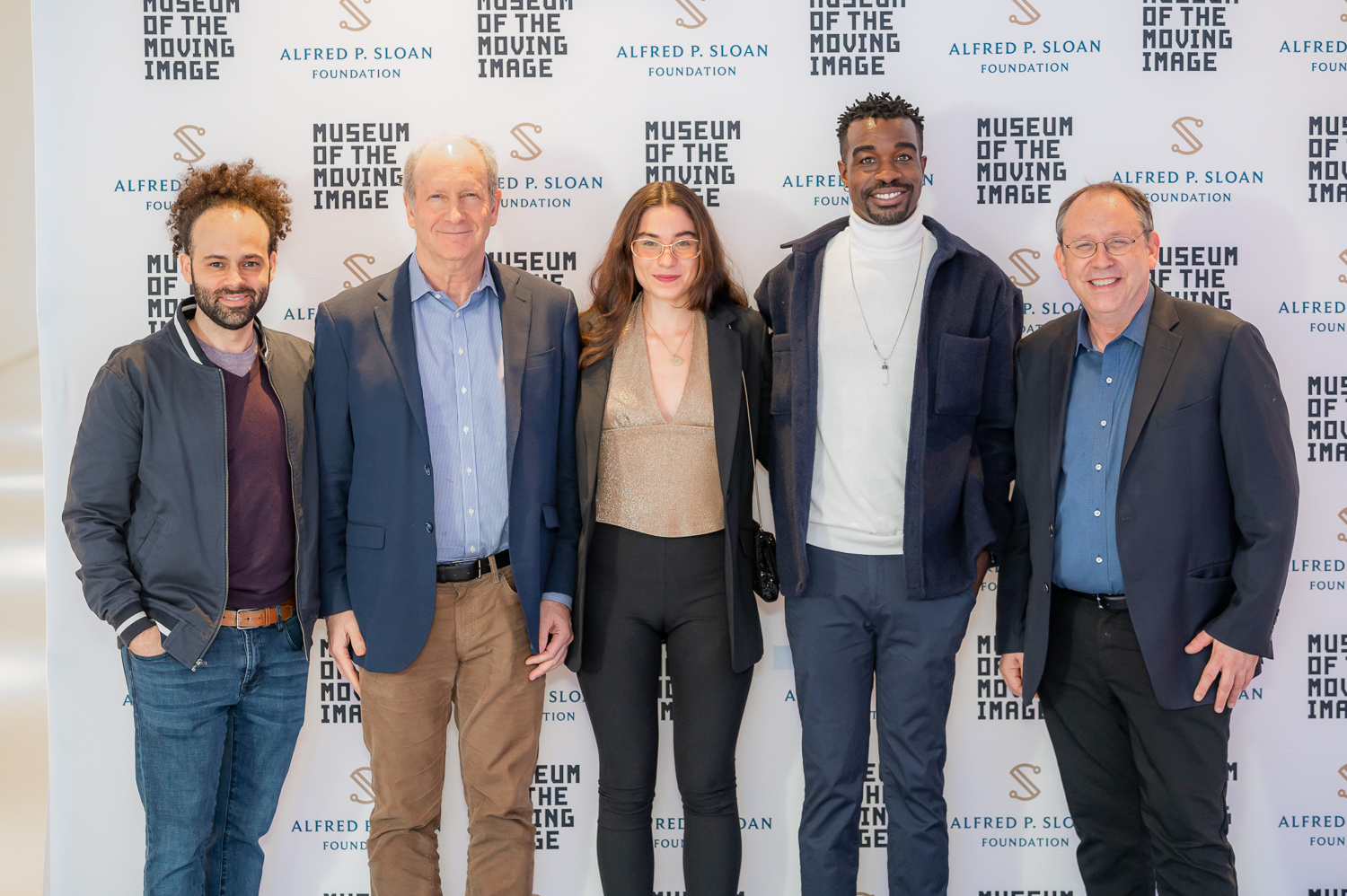Five people stand in front of a step-and-repeat that features logos for Museum of the Moving Image and Alfred P. Sloan Foundation