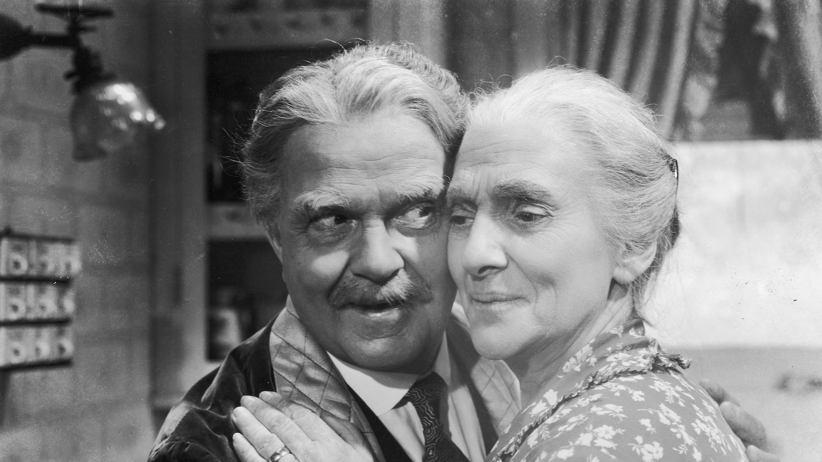 An elderly man and woman hold each other closely, their cheeks touching