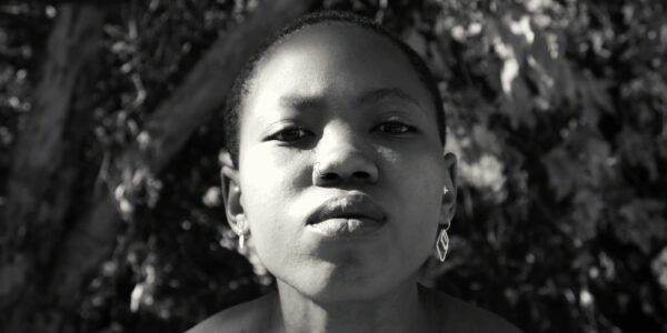 A woman wearing earrings and with short hair stares at the camera in close-up in a black and white image.