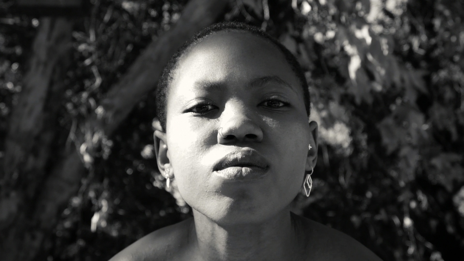 A woman wearing earrings and with short hair stares at the camera in close-up in a black and white image.